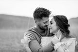 Couple sitting in a field holding and looking at each other.